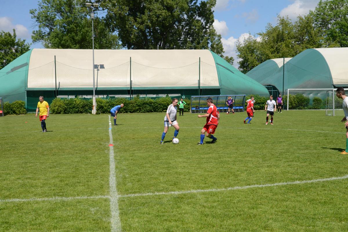 Zdjęcie nr: 11-DSC_3248 przedstawia odbywający się na murawie mecz piłkarski drużyn ubranych w jasnoczarne stroje oraz w stroje czerwone. Jeden z mężczyzn ma piłkę przy nodze.  