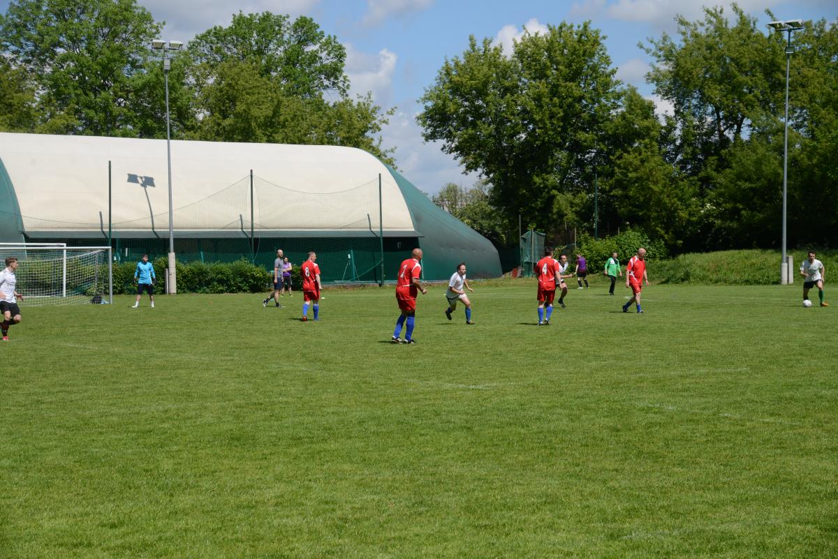 Zdjęcie nr: 14-DSC_3259 przedstawia odbywający się na murawie mecz piłkarski drużyn ubranych w jasnoczarne stroje oraz w stroje czerwone.
