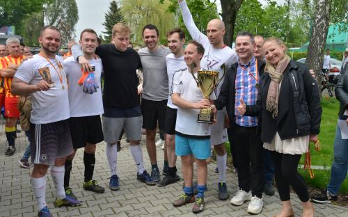 Zdjęcie nr 20: grupa dziesięciu osób: dziewięciu mężczyzn i jedna kobieta, jeden z mężczyzn ma na szyi medal, a w ręku trzyma statuetkę, drugi mężczyzna trzyma w rękach puchar, obok niego stoi mężczyzna z medalem na szyi, kobieta trzyma rękę z uniesionym do góry kciukiem, w drugiej ręce trzyma medale, w tle drzewa oraz grupa osób obserwujących wydarzenie