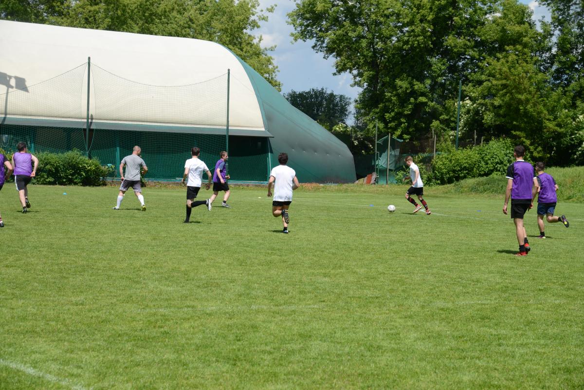 Zdjęcie nr: 22-DSC_3316 przedstawia odbywający się na murawie mecz piłkarski drużyn ubranych w jasnoczarne stroje oraz w stroje fioletowoczarne. Zawodnicy biegają po boisku za  piłką.