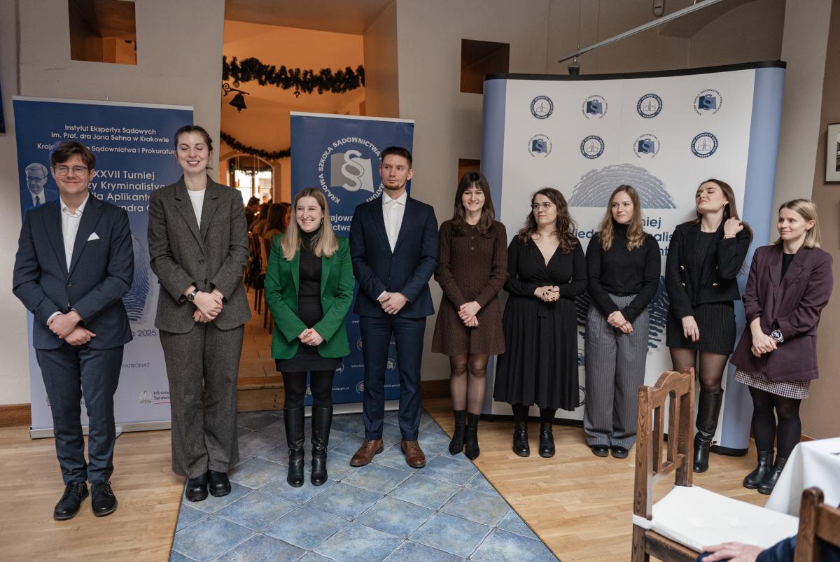 przedstawia wizerunki dziewięciu osób na tle rollup’ów z logo Instytutu Ekspertyz Sądowych im. dra Jana Sehna oraz Krajowej Szkoły Sądownictwa i Prokuratury oraz XXVII Turnieju Wiedzy Kryminalistycznej im. Aleksandra Głazka