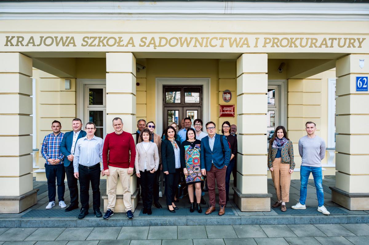 Przed wejściem do budynku Krajowej Szkoły Sadownictwa i Prokuratury  w Lublinie, stoi grupa osób biorących udział w szkoleniu. 