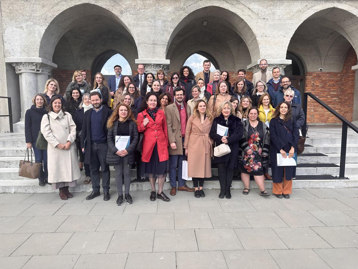 Uczestnicy wydarzenia pozują do grupowego zdjęcia stoją przed budynkami należącymi do Państwowego Muzeum Auschwitz Birkenau